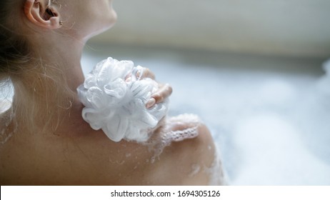 Spa procedure concept. Cropped and back view of young adult woman taking bath, washed back holding sponge in hand and resting in bathroom at home