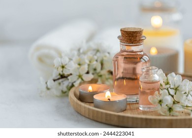 Spa products, aromatherapy, atmosphere of relax. Candles and spa essentials on bamboo tray in bathroom, essential oil, bath salt, towel, sea stone, spring apple tree blooming flowers - Powered by Shutterstock