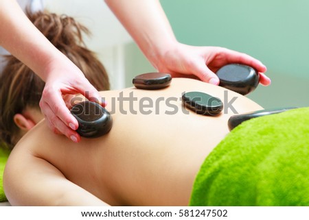 Spa relaxation, healthy pleasure concept. Woman lying on stomach having massage with hot rocks stones in beautician