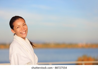 Spa Resort Woman Smiling Wearing Bathrobe Outdoors With Water View On Lake. Beautiful Smiling Happy Mixed Race Chinese Asian / White Caucasian Female Model Outside.