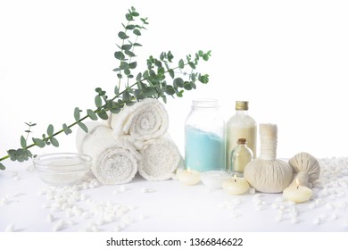 Spa Setting With Eucalyptus Leaves With On Rolled Towel With Oil Bottle ,candle, Herbal Ball On Pile Of White Stones


