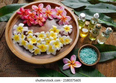 Spa setting with frangipani,, in wooden bowl  , green leaves, ,salt in bowl, oil bottle on mat - Powered by Shutterstock