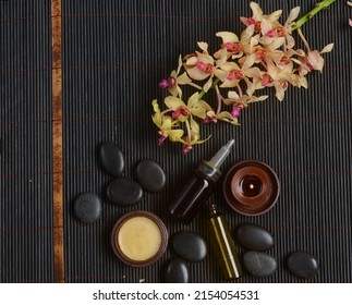 Spa setting with orchid with oil bottle, candle, stones, on bamboo mat.

