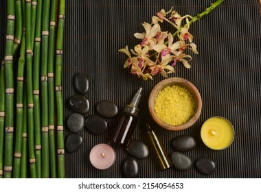 Spa setting with orchid with oil bottle, candle, stones, with bamboo grove on bamboo mat.

