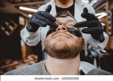 Spa And Skin Care For Men. Barber Professional Applies Black Charcoal Mask To Client Man.