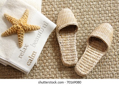 Spa Slippers On Seagrass Carpet With Towels And Starfish