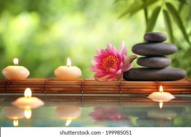 Spa still life with burning candles,zen stone and bamboo mat reflected in a serenity pool
