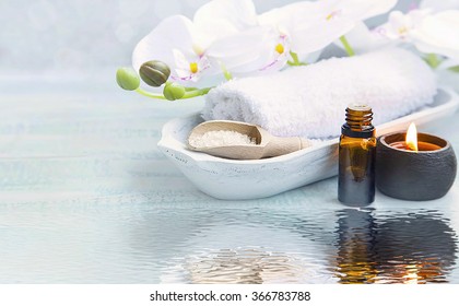 Spa still life with towel,white orchid,sea salt,bath oil and candle on water reflection