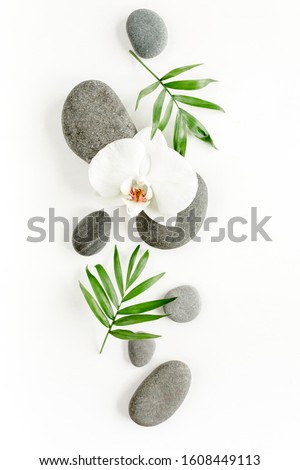 Spa stones, palm leaves, candle and zen like grey stones on white background. Flat lay, top view
