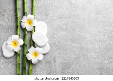 Spa Stones, Plumeria Flowers And Bamboo Stems On Light Grey Table, Flat Lay. Space For Text