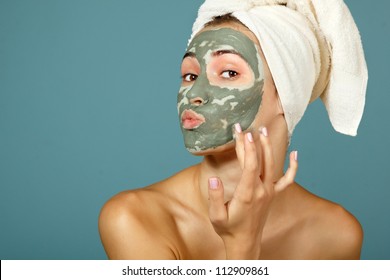 Spa teen girl applying facial clay mask. Beauty treatments. Over blue background.