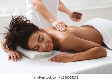 Spa Therapist Applying Exfoliating Body Mask On Sleeping Black Woman Back At Luxury Spa, Body Care Concept. African American Relaxed Lady Having Skin Scrubbing Procedure At Spa Salon