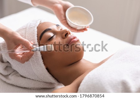 Spa therapist applying face mask on african woman skin, closeup