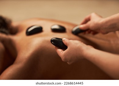 Spa therapist putting hot stones on back of young woman - Powered by Shutterstock