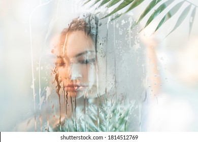 Spa therapy. Natural skincare. Double exposure of sensual peaceful woman face silhouette with exotic green leaves behind wet steamed glass with holographic iridescent blur glow. Body care freshness.