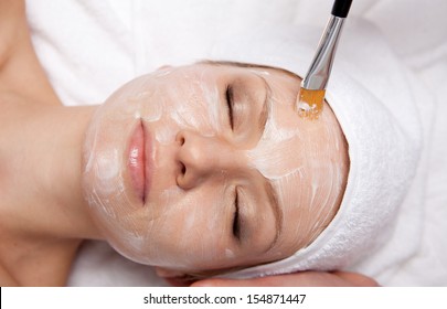 Spa therapy for young woman receiving facial mask at beauty salon
