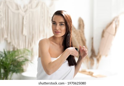 Spa Treatments At Home During Covid-19 Lockdown For Health Of Long, Sleek Hair In Morning. Smiling Millennial Pretty Woman Wrapped In Towel, Combing With Comb, In Bright Modern Boho Bedroom Interior