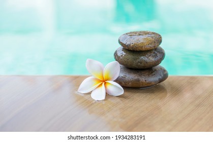 Spa and wellness concept background, Plumeria flower and stone on swimming pool edge with space on blurred blue water background, tropical and summer season
