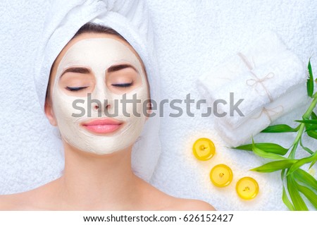 Spa Woman applying Facial clay Mask. Beauty Treatments. Close-up portrait of beautiful girl with a towel on her head applying facial mask.