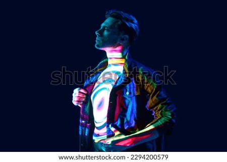 Space inside. Handsome young man standing with circle shape multicolor, neon, digital lights reflection on body over dark background. Concept of modern photography, art, cyberpunk, techno, creativity