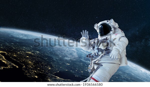 Space man astronaut greets and waves his hand in\
space on a background of the blue planet Earth. Space mission\
wallpaper, concept. Welcome to\
space