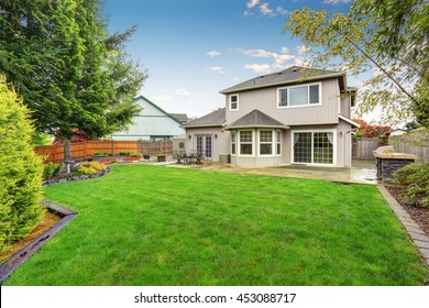  Spacious backyard garden of large beige house with green lawn and Cozy patio area. 