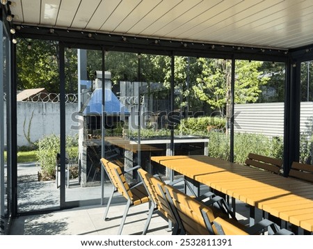 A spacious barbecue area with a canopy made from natural materials, enclosed. A patio with a table and chairs, sitting under a roofed structure.