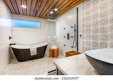 Spacious bathroom with tub and shower in enclosure glass walls black bathtub tiger wood accents decorative tile and mosaic floor tile