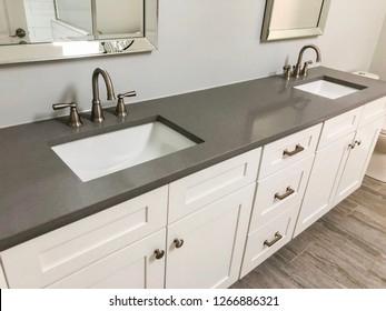 Spacious bathroom vanity counter top in gray tones with tile floors, white rectangular sinks, stainless steel mirrors, double handle chrome faucets and wooden white cabinets.