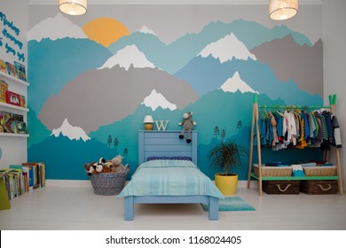 A spacious boy bedroom with a beautiful turquoise and grey mountain wall mural and bookshelves