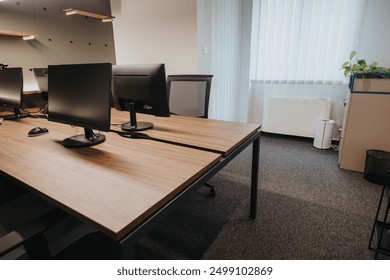 Spacious and bright office featuring two computer monitors on a large wooden desk, minimalist decor, and comfortable workspace ambiance.