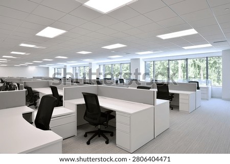 Spacious and bright office interior featuring rows of cubicles, ergonomic chairs, and large windows allowing ample natural light.