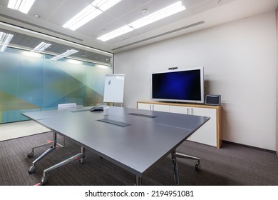 A Spacious, Bright Office Meeting Room With Gray Flooring, A Glass Wall And A Large Table.