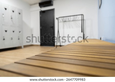 A spacious changing room features a long wooden bench and lockers along the wall. The minimalist design creates a clean and organized atmosphere, perfect for visitors.