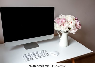 Spacious clean workspace. On the table is a computer and flowers peonies.