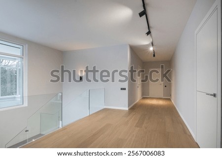 A spacious corridor on the second floor of a country house. Finishing, beige laminate, stairs with glass railings.