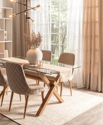 Spacious Dining Room In Nordic Style Showcasing A Sleek Glass Tabletop, Fabric Quilted Chairs, An Intricate Chandelier, And Ambient Sunlight Filtering Through Sheer Curtains, On A Woven Area Rug.