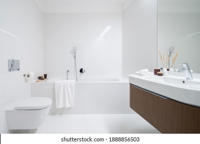 Spacious and elegant bathroom with big bathtub, white tiles, washbasin with wooden cabinet with drawer and big mirror - Powered by Shutterstock