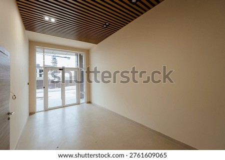 Spacious empty commercial interior featuring large windows and a wooden ceiling, with neutral walls and tiled flooring, ready for customization