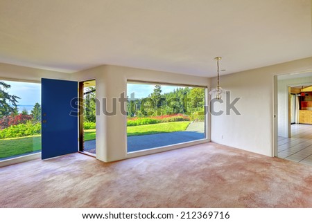 Spacious empty dining and living room with panorama windows. overlooking beautiful water view of Puget Sound. Soft pink brown carpet floor. Unique modern old home build in 1952.