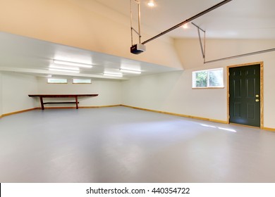 Spacious Empty Garage Interior With Green Door, Small Window And Vaulted Ceiling.
