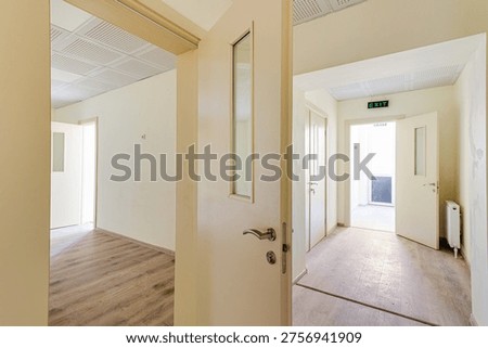 Spacious empty hall or office space featuring beige walls, professional acoustic ceiling tiles, wooden laminate flooring, and several windows with radiators in a new building.