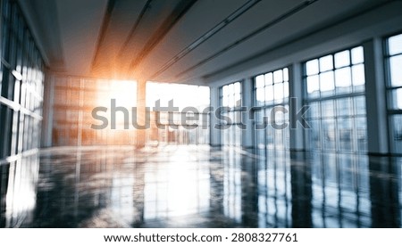 A spacious and empty modern office interior with a polished floor reflecting the bright sunlight entering through expansive glass windows.