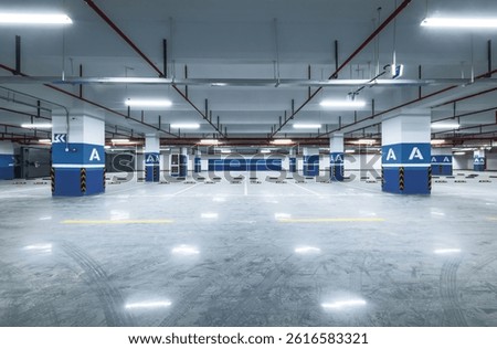 Spacious empty modern underground parking lot garage interior with concrete floor blue pillars and bright lighting.