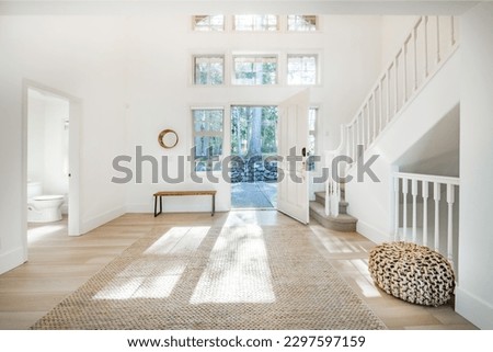 spacious foyer entry to an entry with dappled sunshine jute ottoman wooden bench open door with bright light shining in to a dual white wood railed stairway