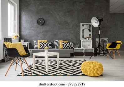 Spacious, grey living room with sofa, chairs, standing lamp, small coffee-table, decorations in yellow, black and white 