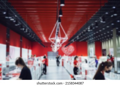 A spacious hall of a jewelry store with a red and white interior and saleswomen standing behind the counters. Defocused photo.