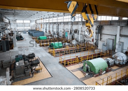 Spacious industrial interior features high-pressure air turbo compressors and turbo expanders within chemical enterprise. Yellow overhead crane with massive hook hangs above organized factory floor.