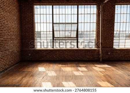 Spacious industrial loft with large windows, exposed brick walls, and wooden floors, flooded with natural light.
