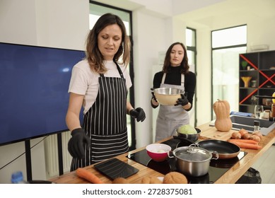 In a spacious kitchen filled with light, two chefs collaborate on meal preparation. One chops ingredients while the other holds a bowl, showcasing teamwork in culinary arts.